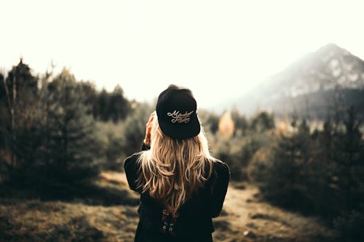 A woman in black cap and sweater enjoys a mountain view, embracing outdoor adventure.